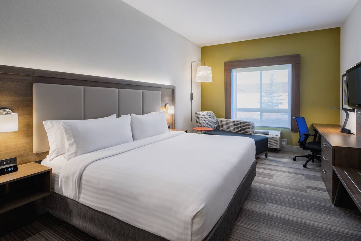 A hotel room with a large bed, a desk with a chair, a television, and a window with a view.
