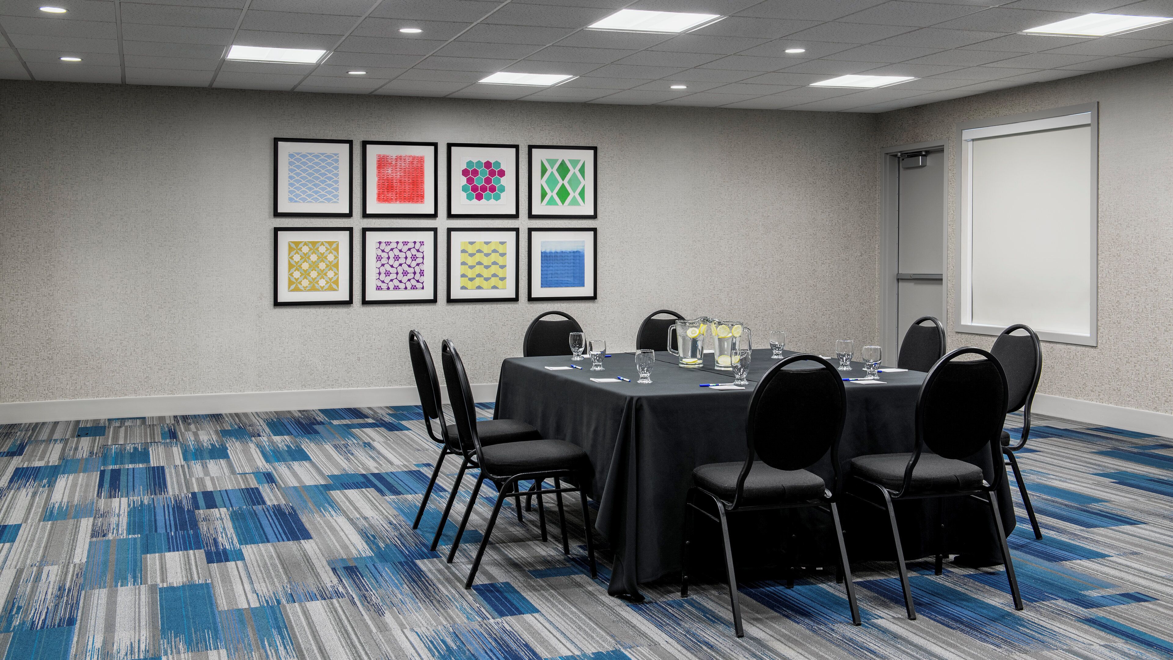 A conference room with a round table, black chairs, and a carpeted floor.