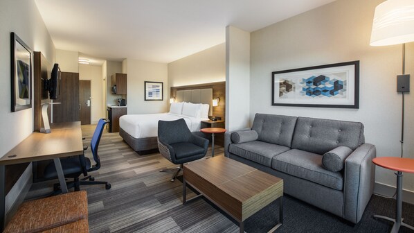 Ein Hotelzimmer mit einem Bett, einem grauen Sofa, einem Holztisch, einem Schreibtisch mit Stuhl und einem kleinen Tisch mit Lampe.