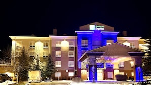 A Holiday Inn Express hotel with a central entrance, multiple floors, and a parking area with vehicles and snow.