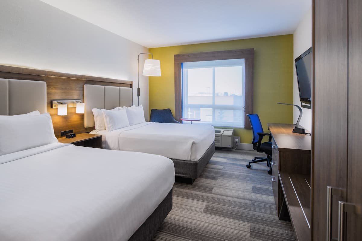 A hotel room with two beds, a desk with a computer, a chair, a TV, and a window with a view.
