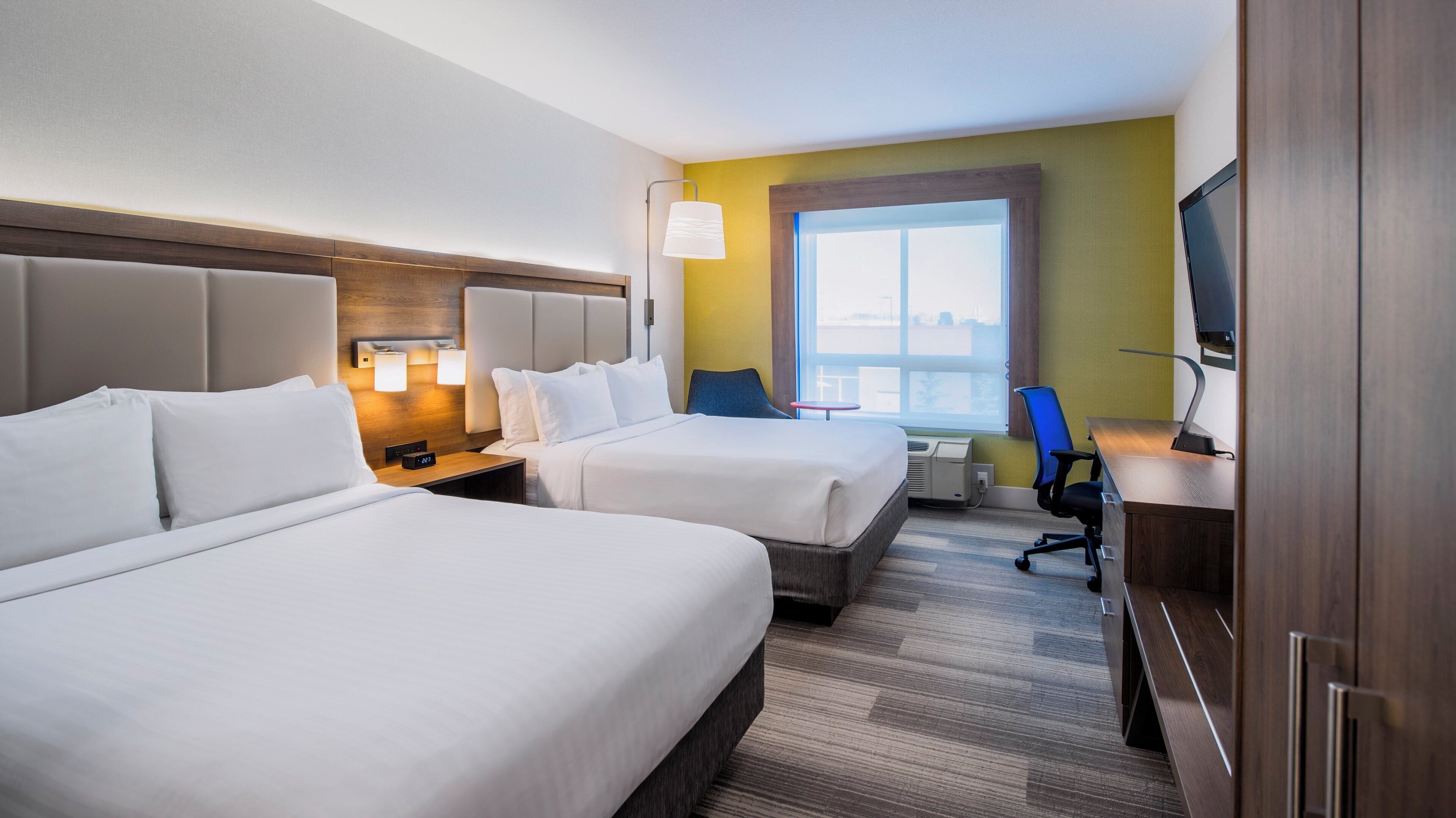 A hotel room with two beds, a desk, a chair, a TV, and a window with a view.