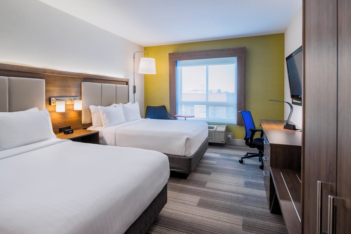 Een hotelkamer met twee bedden, een bureau, een stoel, een televisie en een raam met uitzicht.