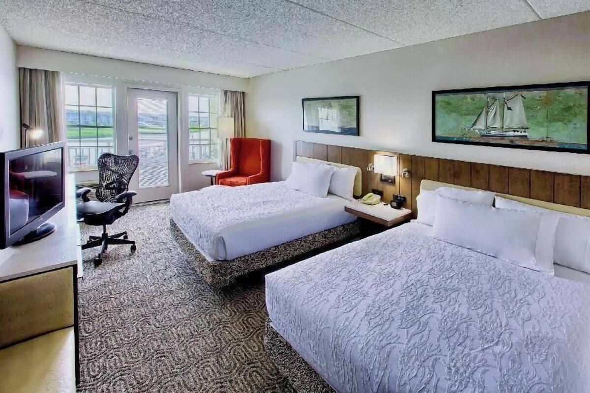 A hotel room with two beds, a TV, a desk, a chair, and a painting.