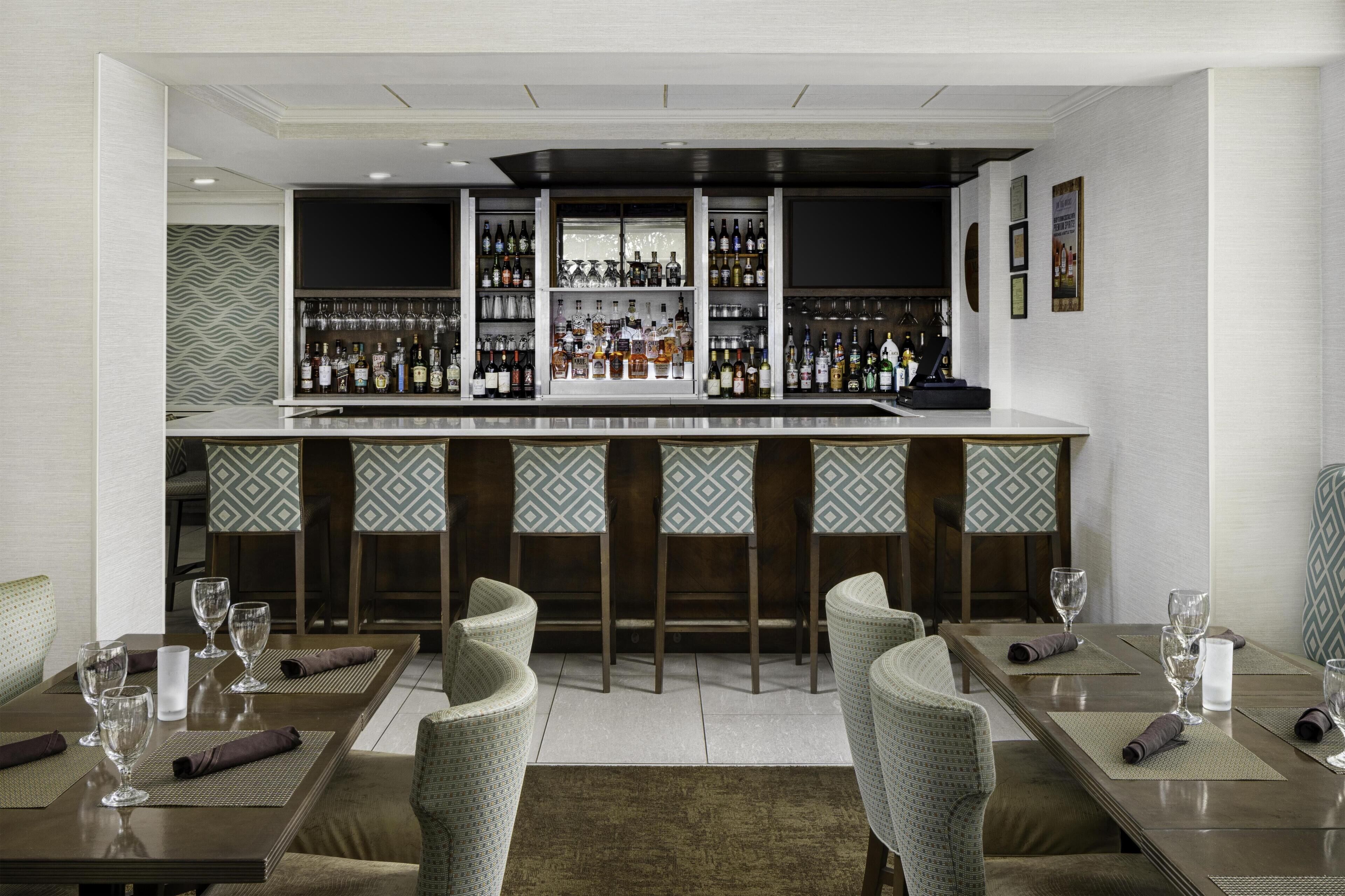 A bar area with a long counter, multiple shelves of bottles, and bar stools.