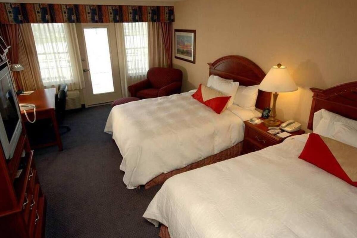 A hotel room with two beds, a desk, a chair, a TV, and a window with curtains.
