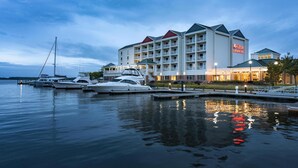 Un hôtel situé au bord de l’eau, doté de nombreux balcons, un port de plaisance avec des yachts et une façade bien éclairée.
