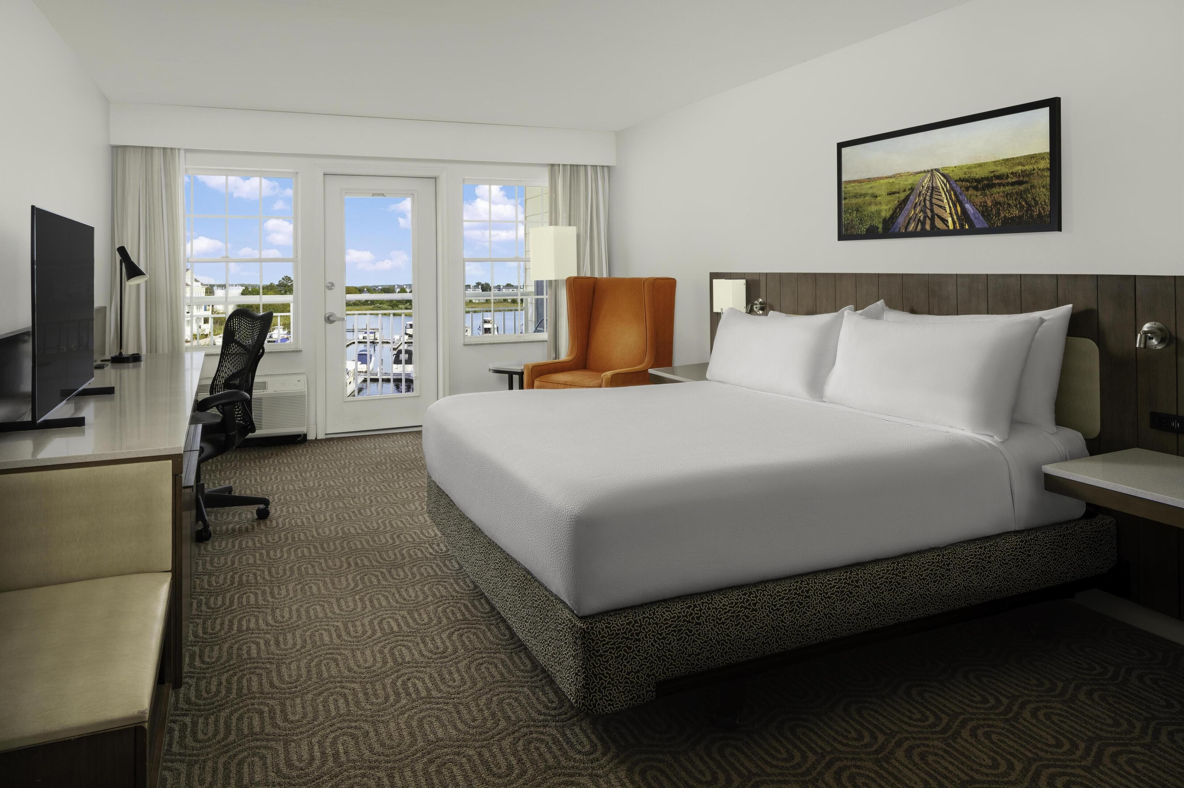 Habitación de hotel con una cama grande, un escritorio con computadora, una silla y vista al exterior.