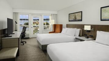 A hotel room with two beds, a desk, a TV, and a view of the outdoors.