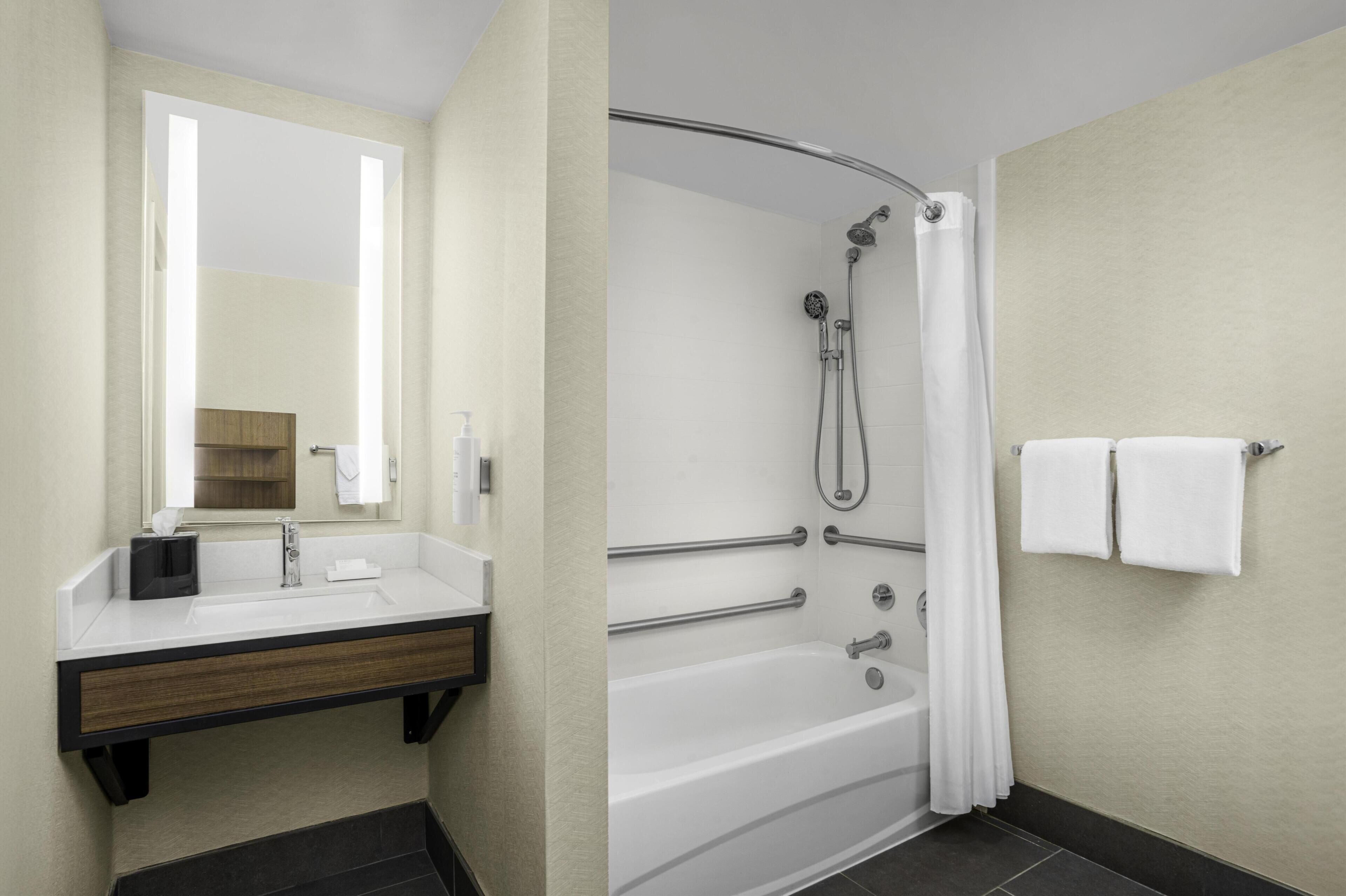 A modern bathroom with a sink, mirror, and bathtub.