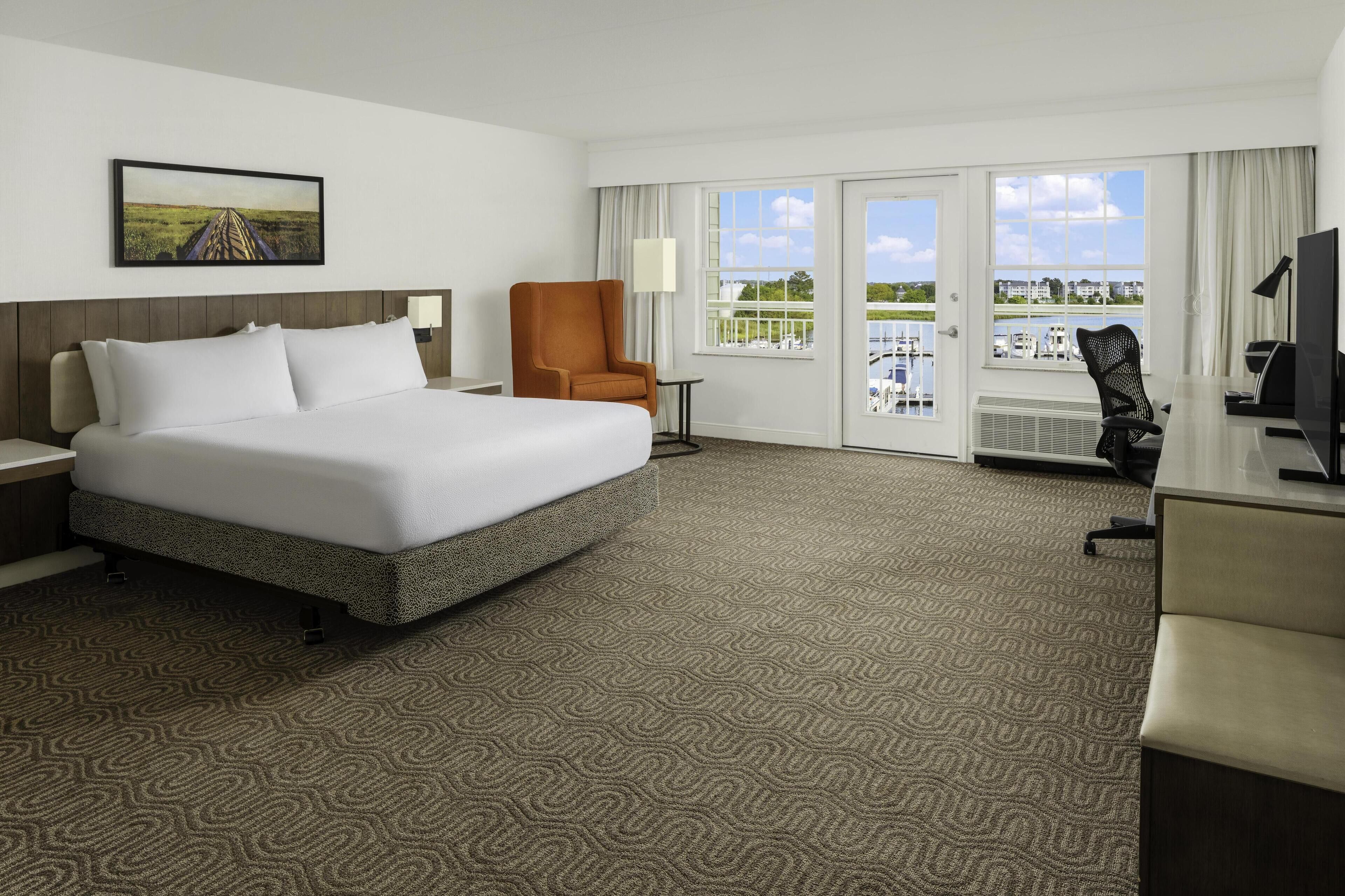 Habitación de hotel con una cama grande, un escritorio con silla, televisión y vistas al exterior.