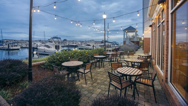 Une terrasse avec des sièges extérieurs, donnant sur une marina où sont amarrés des bateaux.