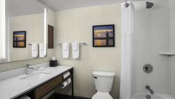 A modern bathroom with a white sink, vanity, and toilet. There are two framed pictures on the wall, a shower curtain, and a bathtub.