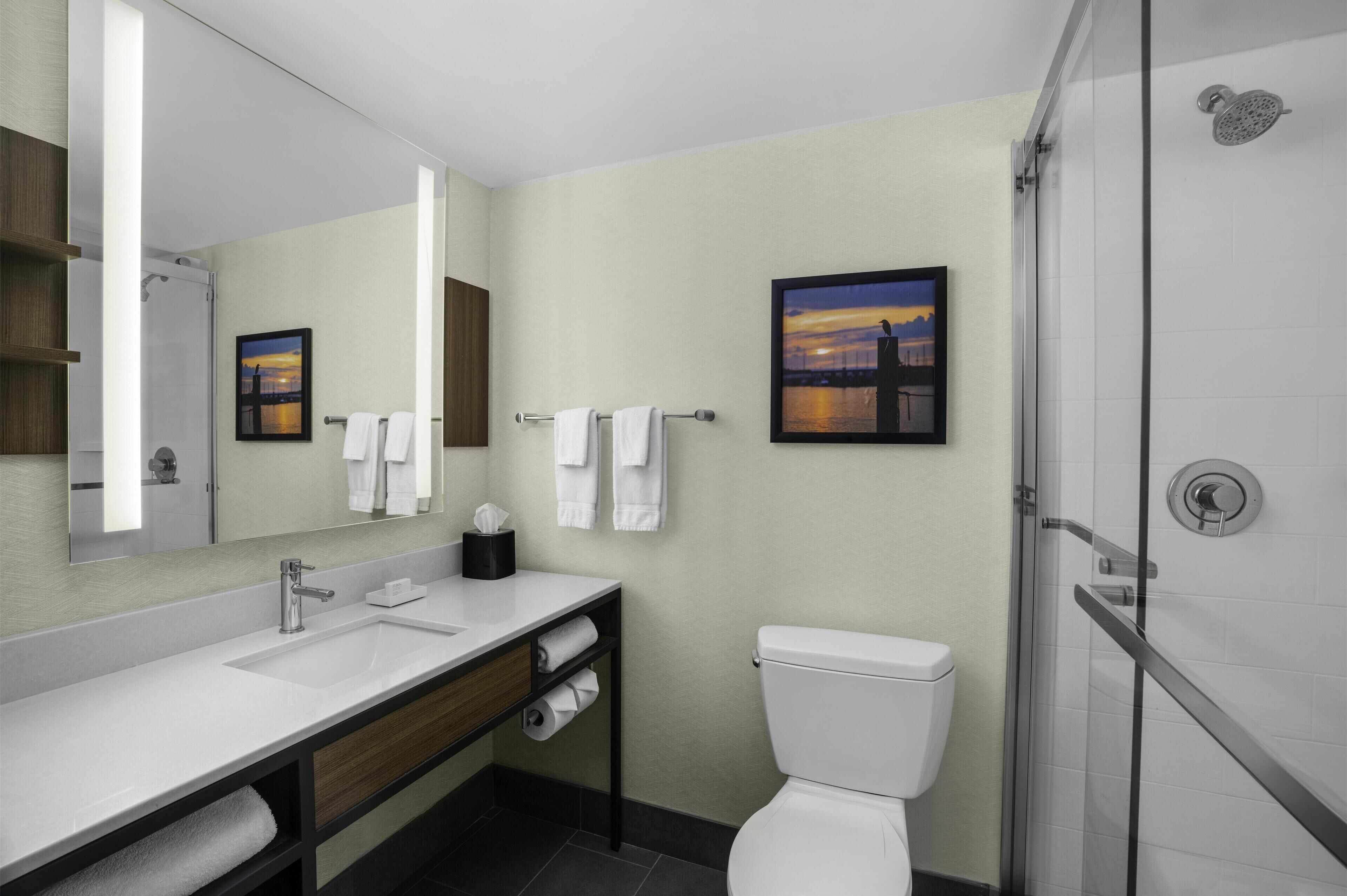 A modern bathroom with a large mirror, a sink, a toilet, and a shower.
