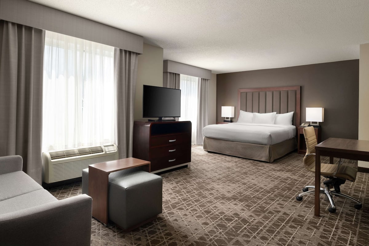A hotel room with a bed, a desk, a chair, a television, and a window with curtains.