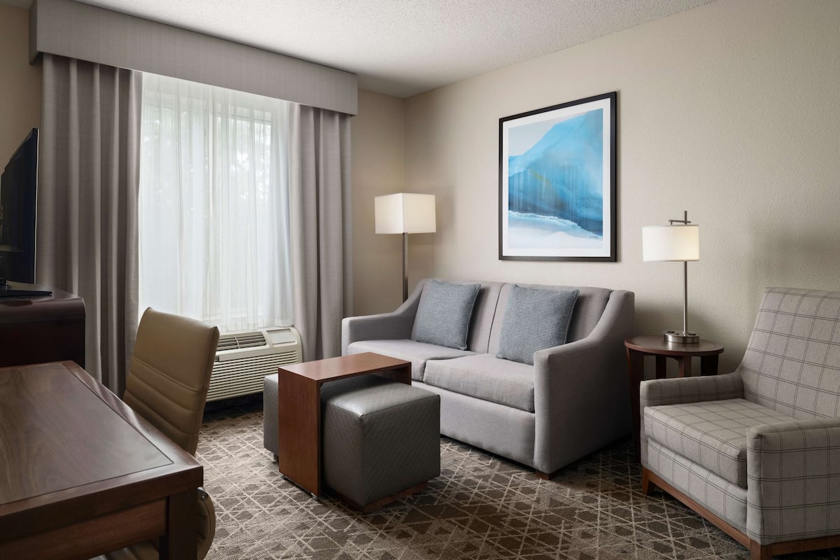 A hotel room with a sofa, armchair, coffee table, and a TV.