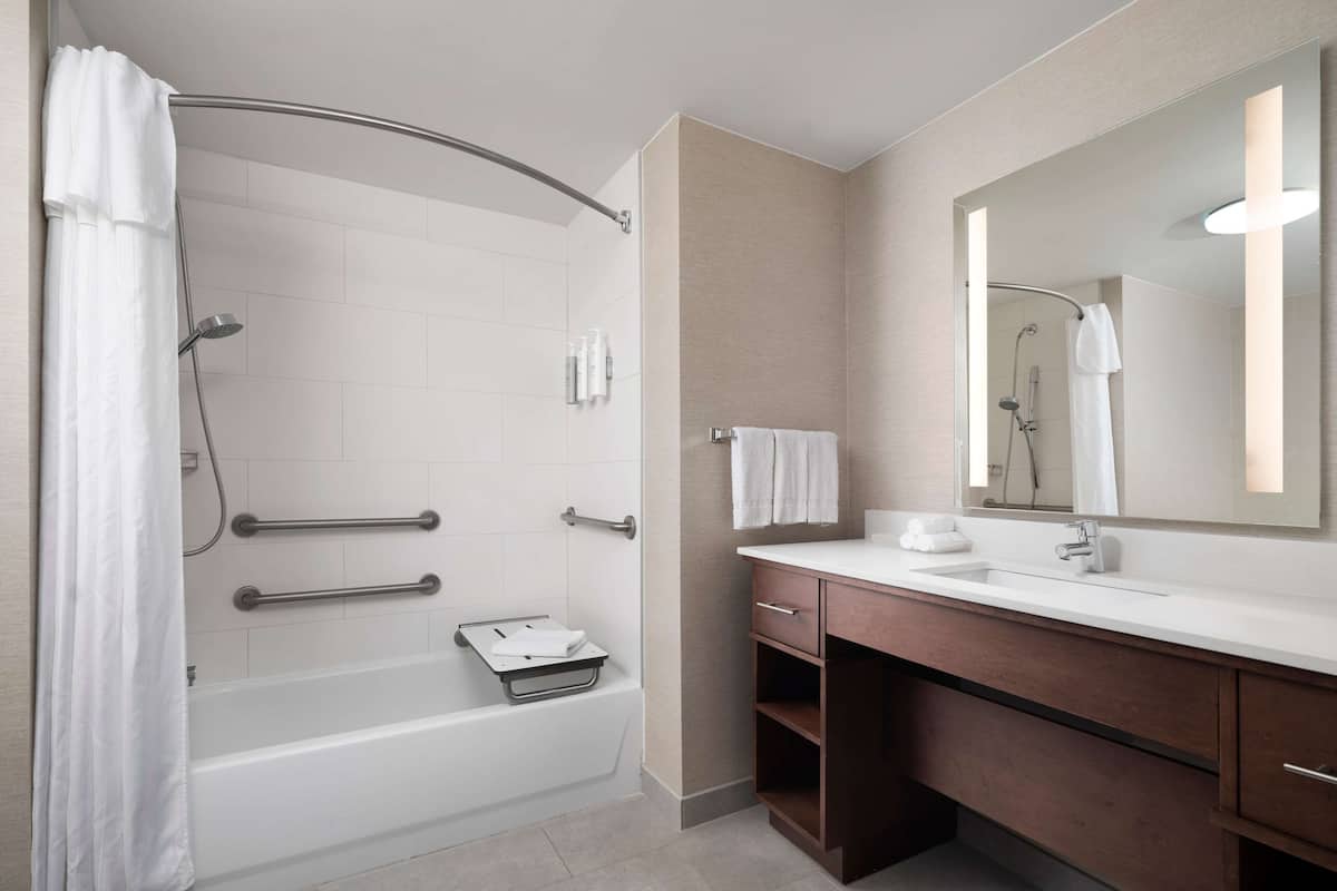A modern bathroom with a bathtub, a shower, a vanity with a mirror, and a towel rack.