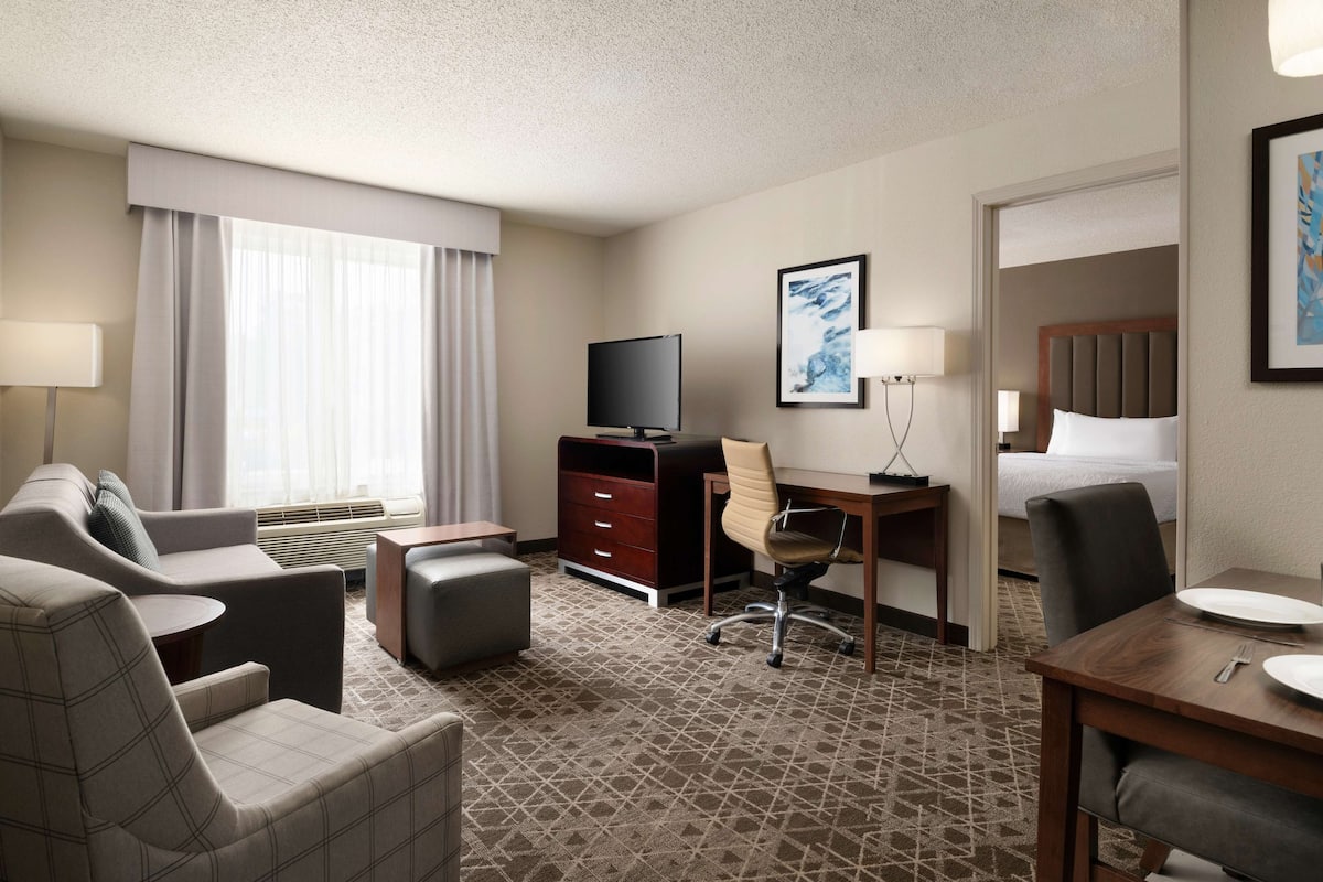 A hotel room with a sofa, a desk, a television, a chair, a bed, and a dining table.