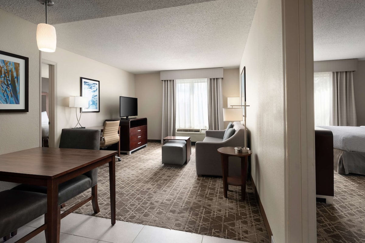 A hotel room with a bed, a desk, a chair, a sofa, a TV, and a lamp.
