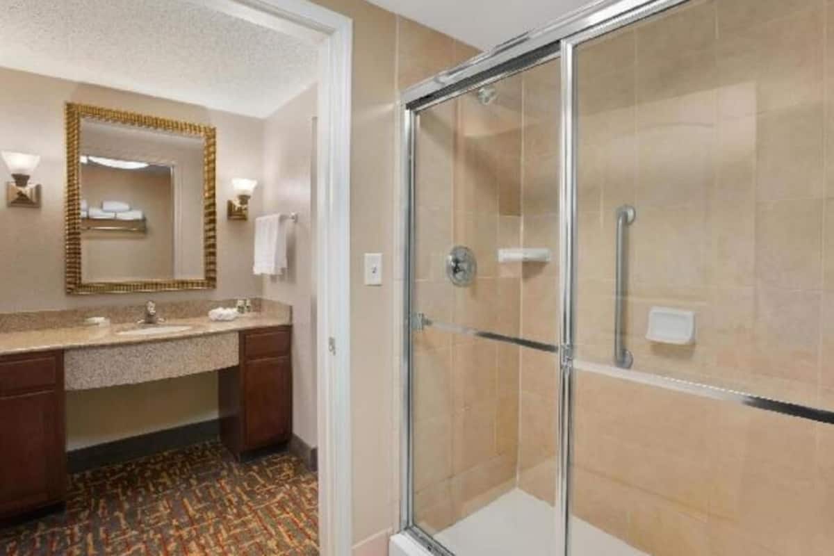 A hotel bathroom with a shower, a sink, and a mirror.