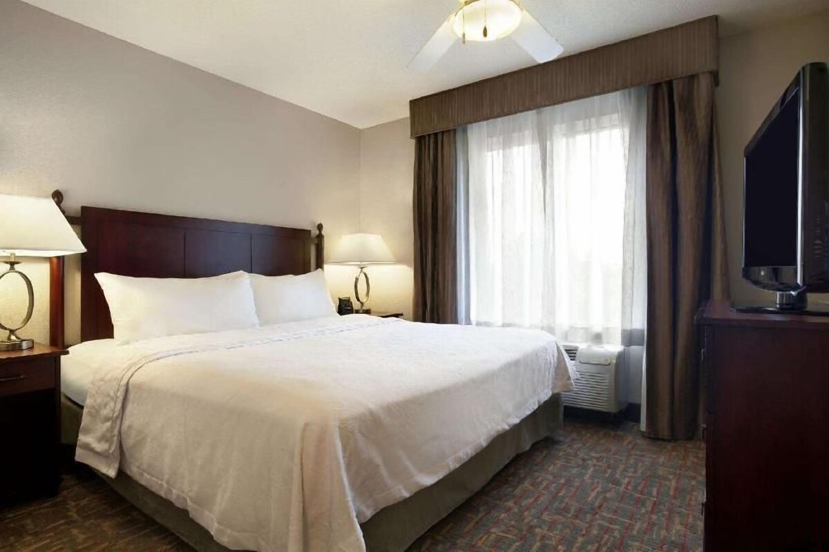 Une chambre d’hôtel avec un grand lit, des lampes de chevet, un téléviseur à écran plat et une fenêtre avec des rideaux.