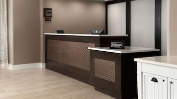 A hotel reception desk with a modern design, a sign indicating Hilton Honors, and a 'Manager on Duty' sign.