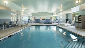 Una piscina interior con sillones y mesas, rodeada de ventanas y un suelo de baldosas.