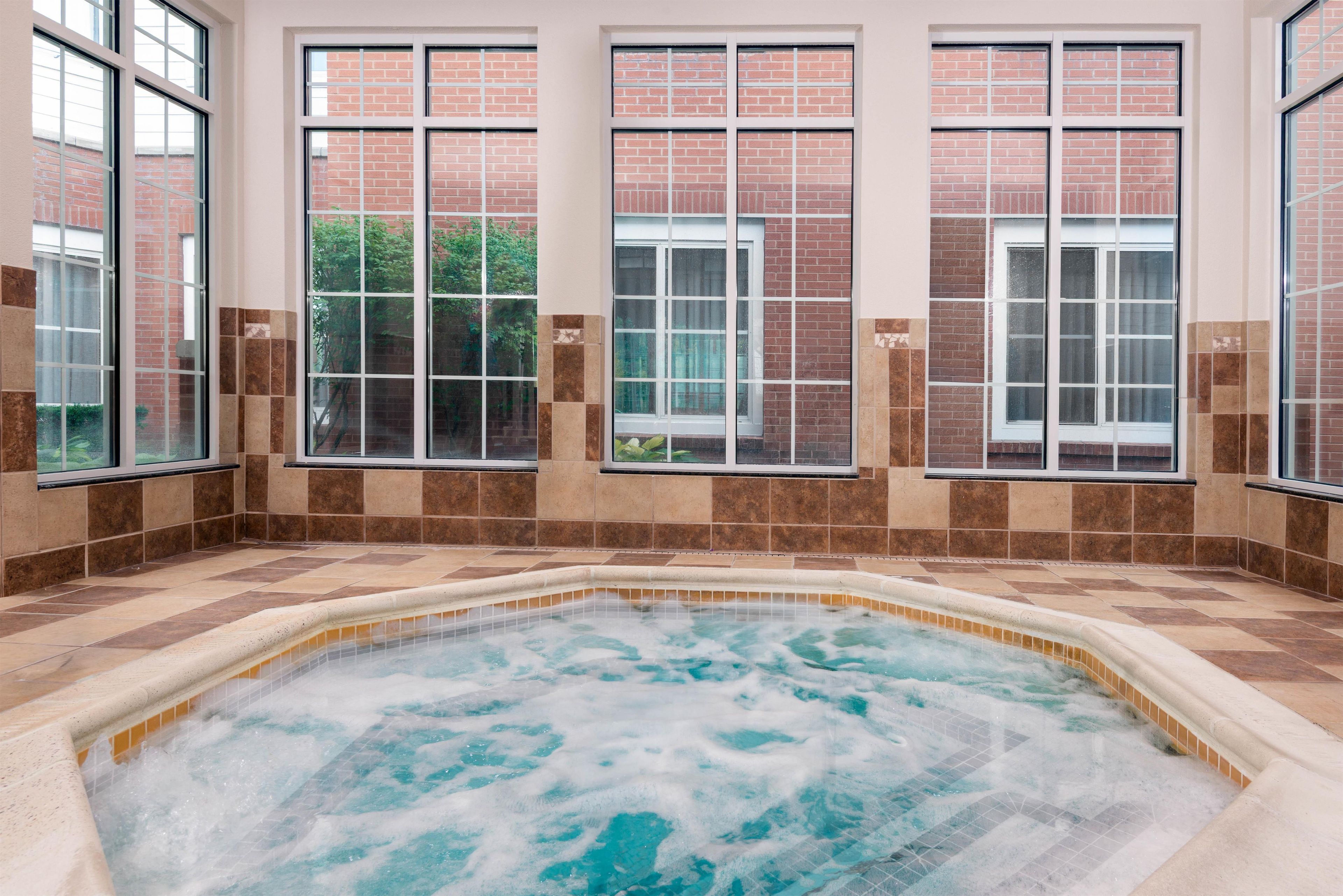 Un jacuzzi con piso de baldosas y amplias ventanas con paredes de ladrillo.