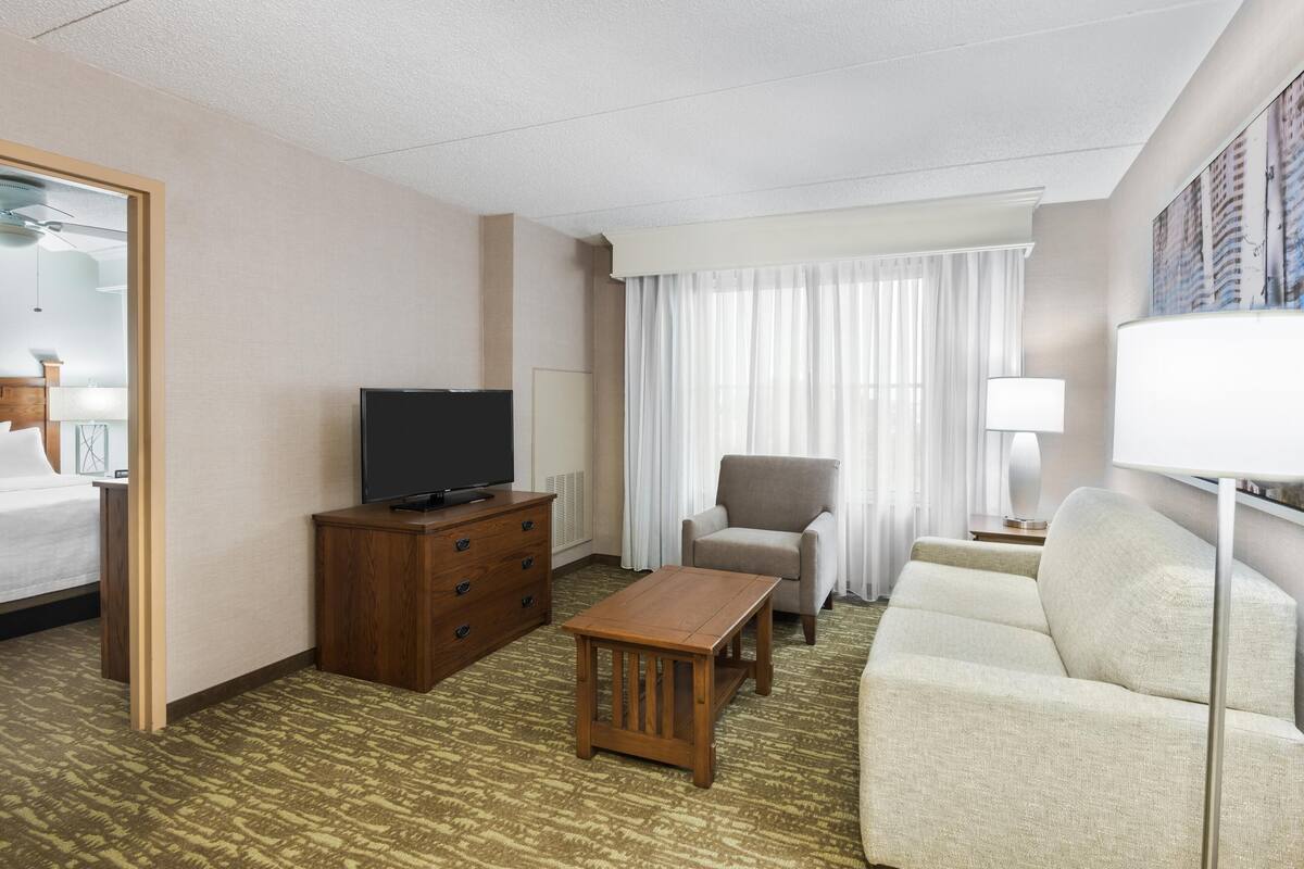 Hotelkamer met een bed, een televisie, een houten dressoir, een bank, een salontafel en een raam met gordijnen.