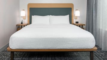 Una habitación de hotel con una cama grande, dos mesitas de noche con lámparas, un cabecero y una ventana con cortinas.