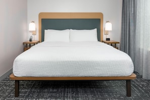Une chambre d’hôtel avec un grand lit, deux tables de chevet avec des lampes, une tête de lit et une fenêtre avec des rideaux.