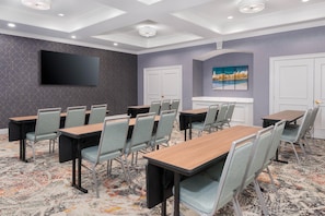 Une salle de conférence équipée d’un t éléviseur à écran plat, de plusieurs tables et de chaises.