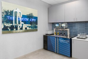 Een hotelbar met een groot bord waarop 'THE QUEEN CITY' staat, een minibar en een scherm dat drankjes laat zien.