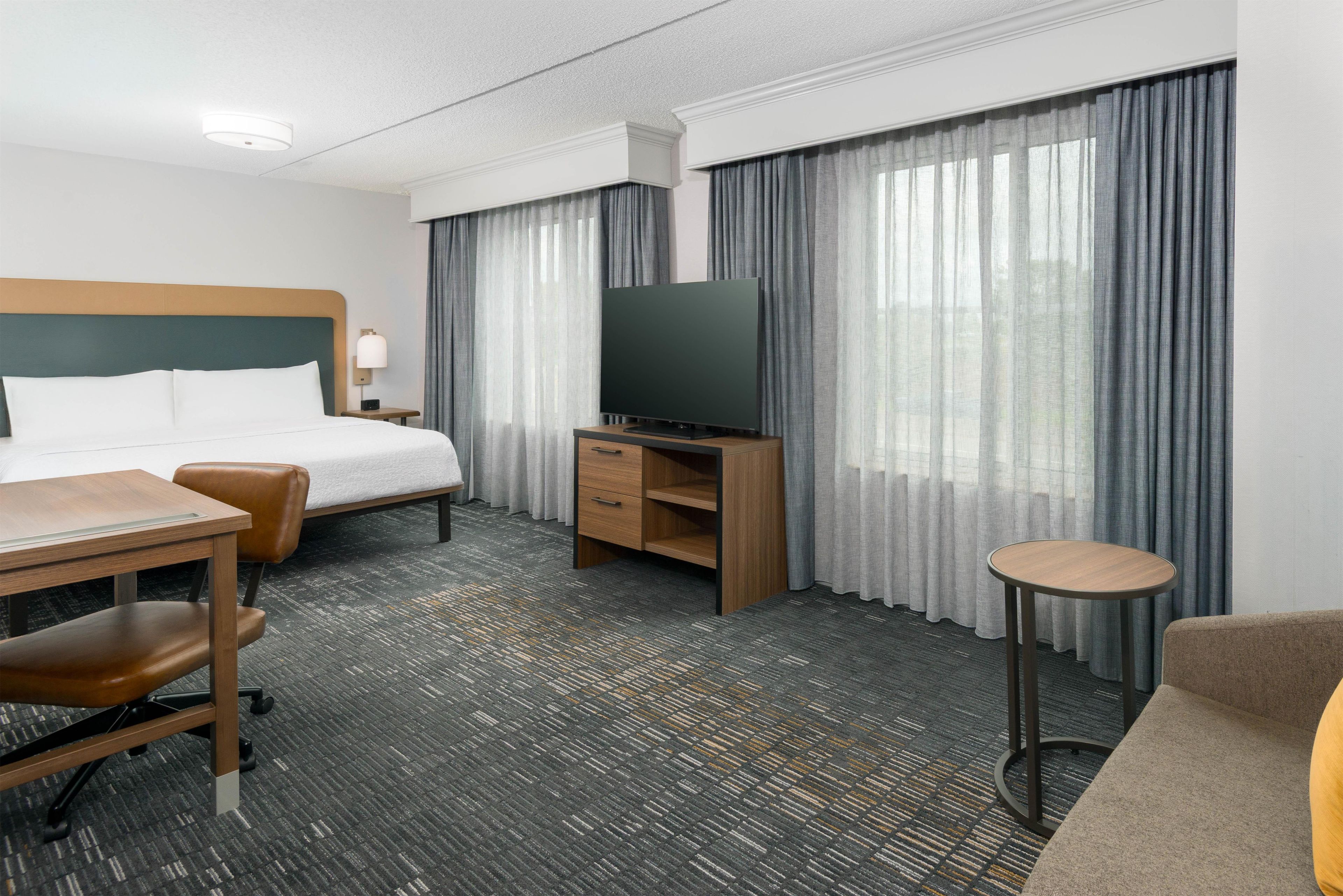 Ett hotellrum med en säng, ett skrivbord, en stol, en tv och ett litet bord.