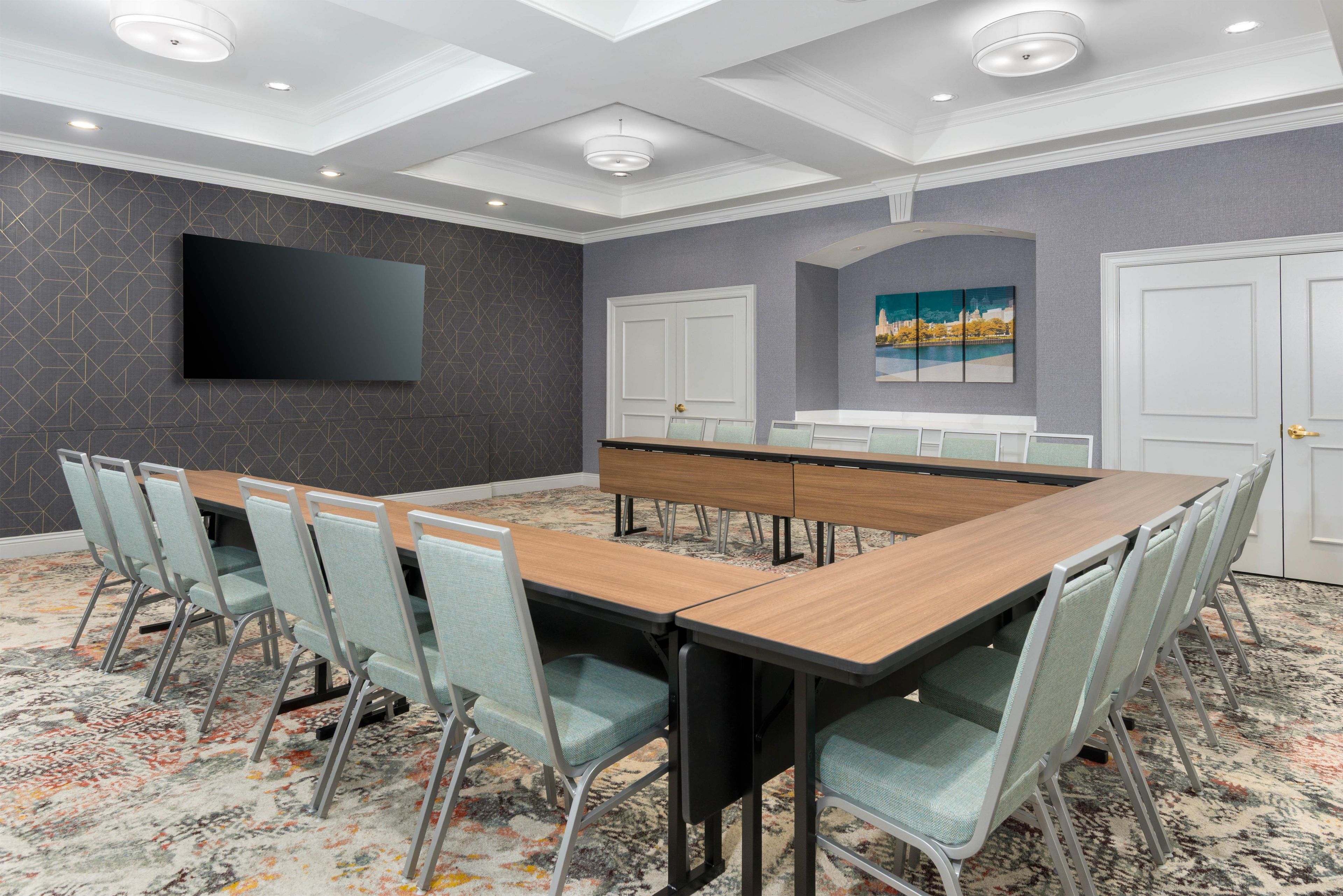 A conference room with a long table, chairs, a flat-screen TV, and a painting on the wall.