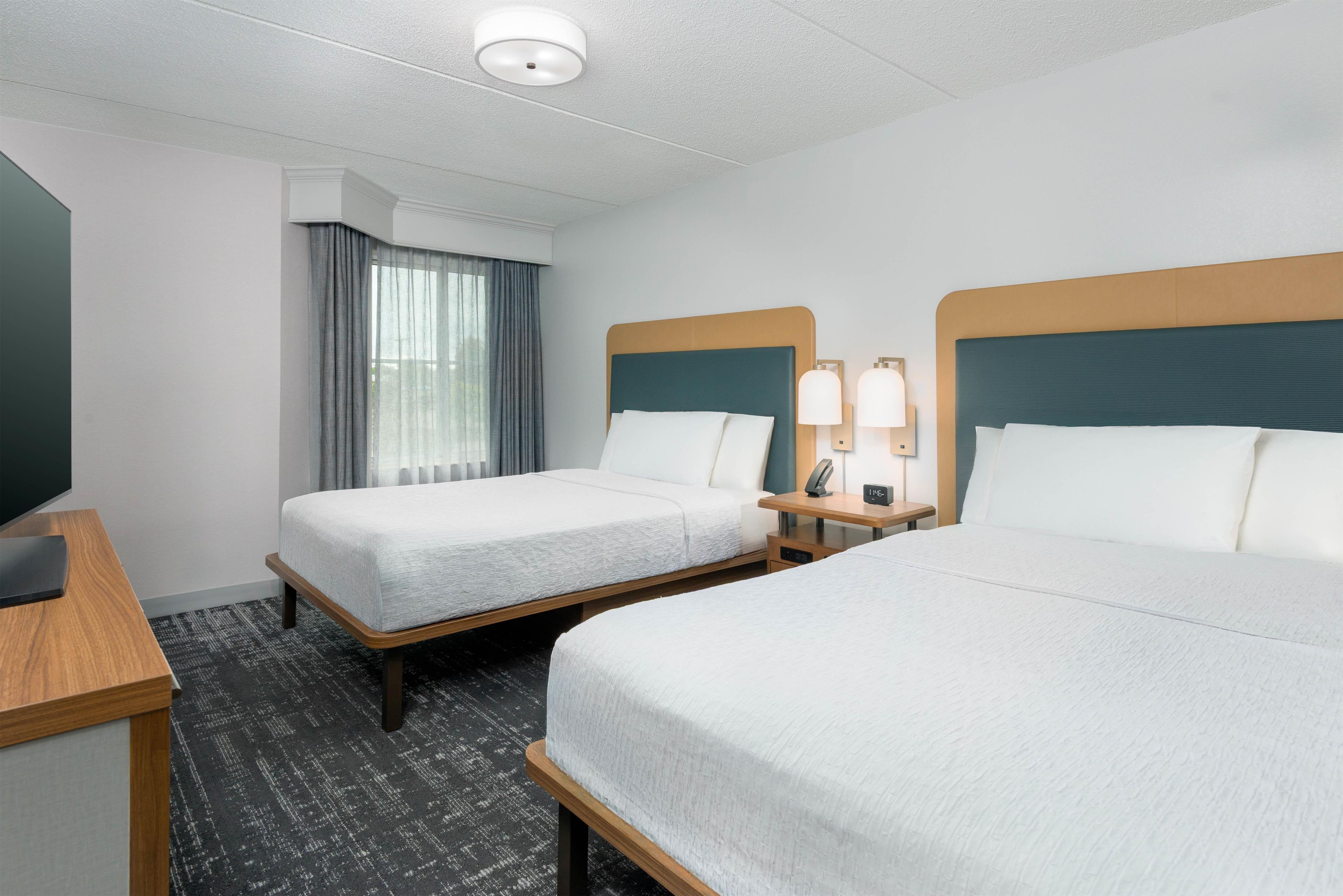 A hotel room with two beds, a desk, a chair, a TV, and a window with curtains.