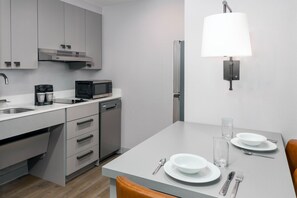 Een moderne keuken met een ingebouwde vaatwasser, een magnetron en een koffiezetapparaat. Er is een eettafel met borden, glazen en bestek.