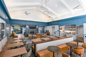 A spacious hotel lobby with multiple seating areas, a bar, and a kitchen visible in the background. - Homewood Suites by Hilton Buffalo/Amherst (Buffalo)