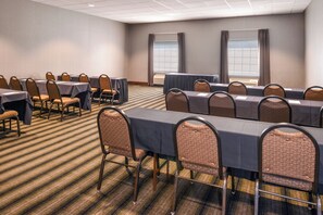 A conference room with multiple tables and chairs, carpeted floor, and large windows with curtains.