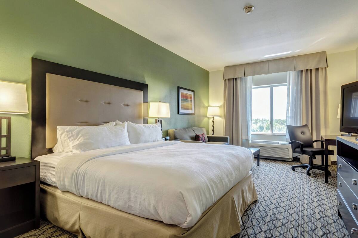 A hotel room with a large bed, two bedside tables with lamps, a desk with a chair, and a television.