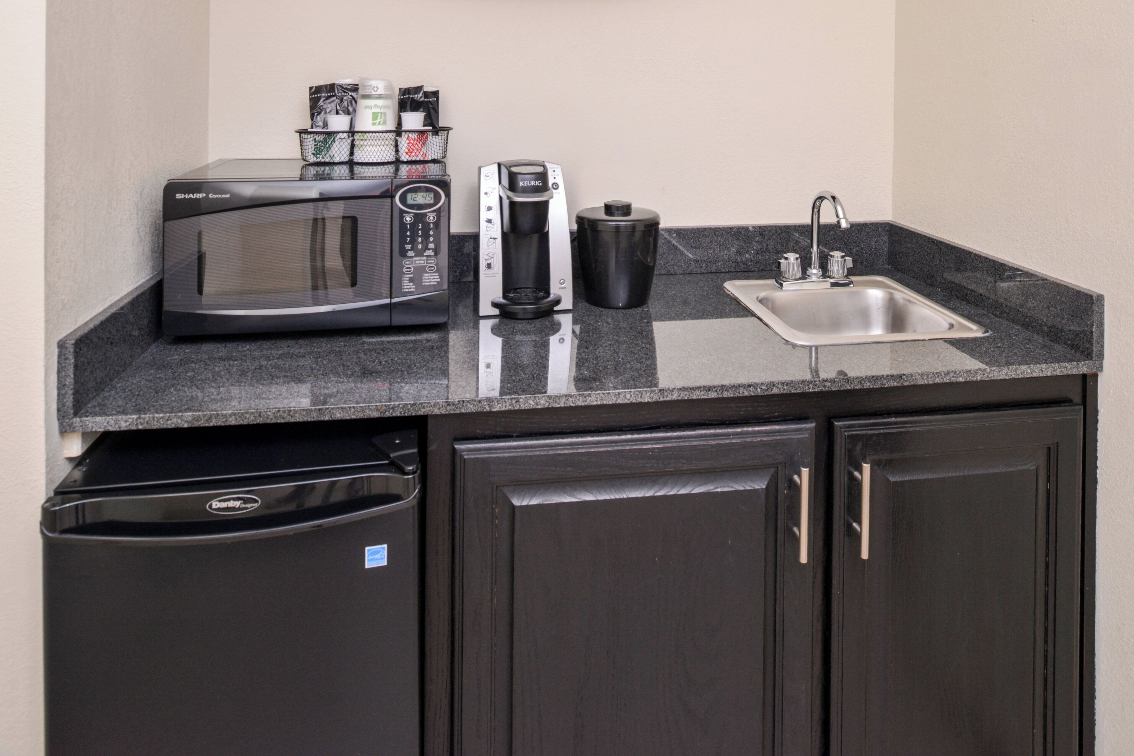 Una kitchenette compacta equipada con microondas, cafetera y lavamanos.