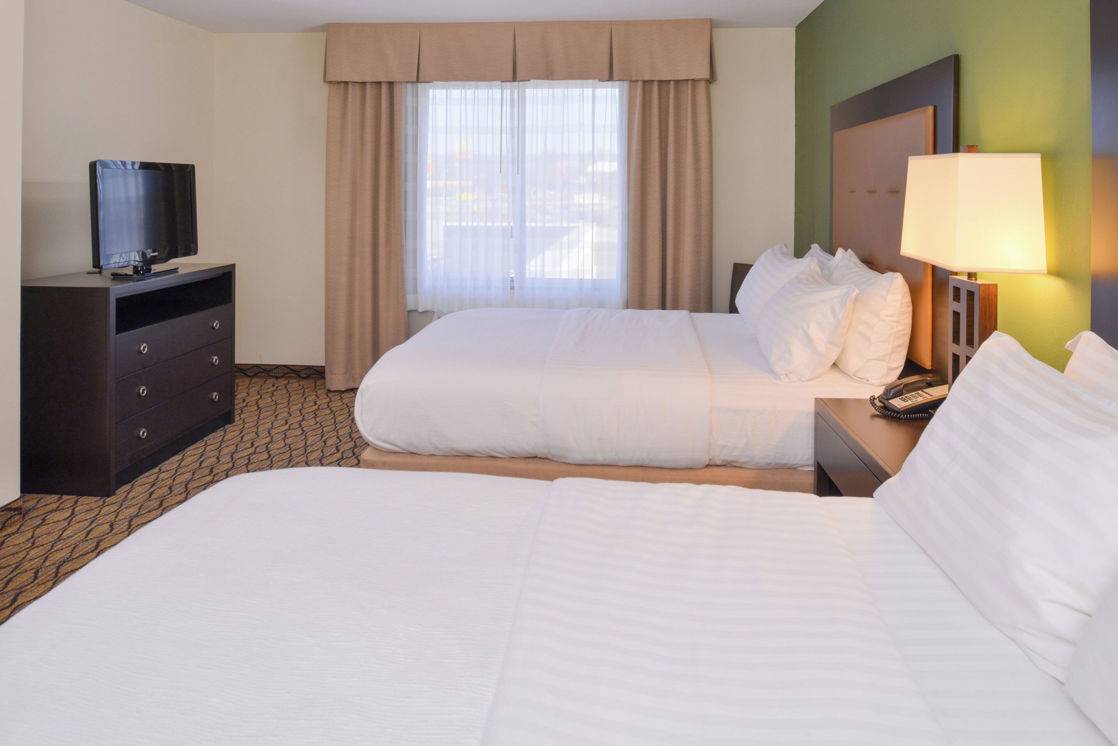 Una habitación de hotel con una cama, un televisor en una cómoda y una lámpara en una mesita de noche.