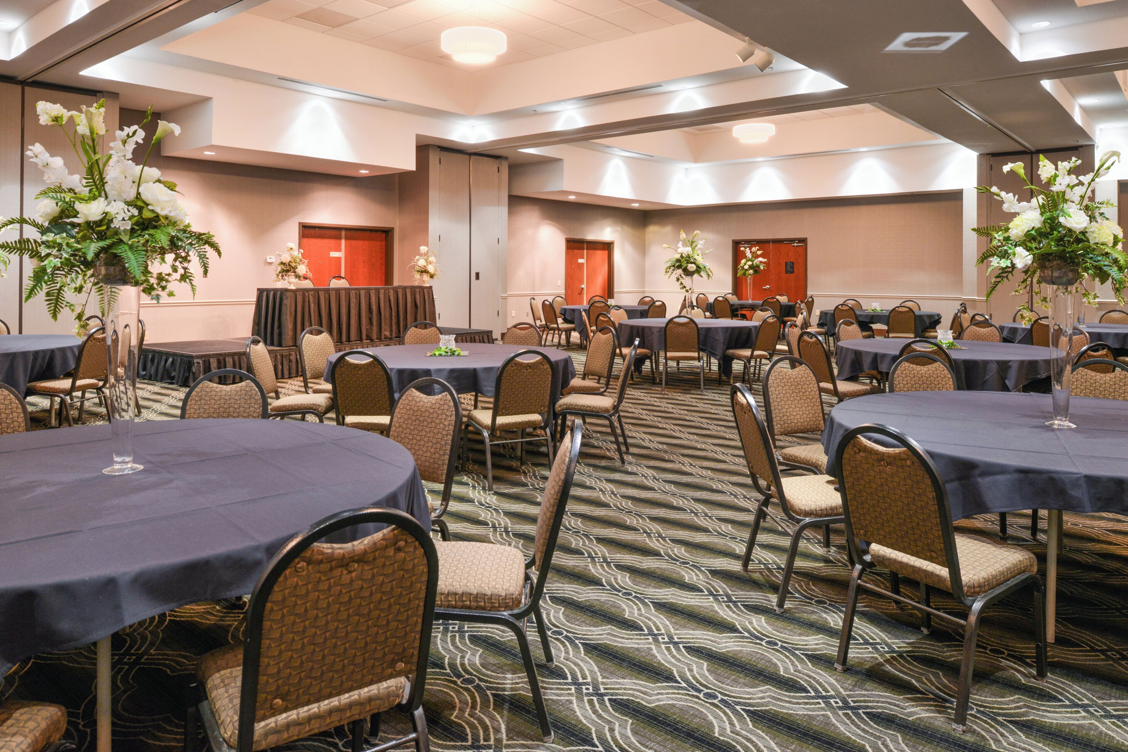 A conference room with multiple round tables, chairs, and floral centerpieces.