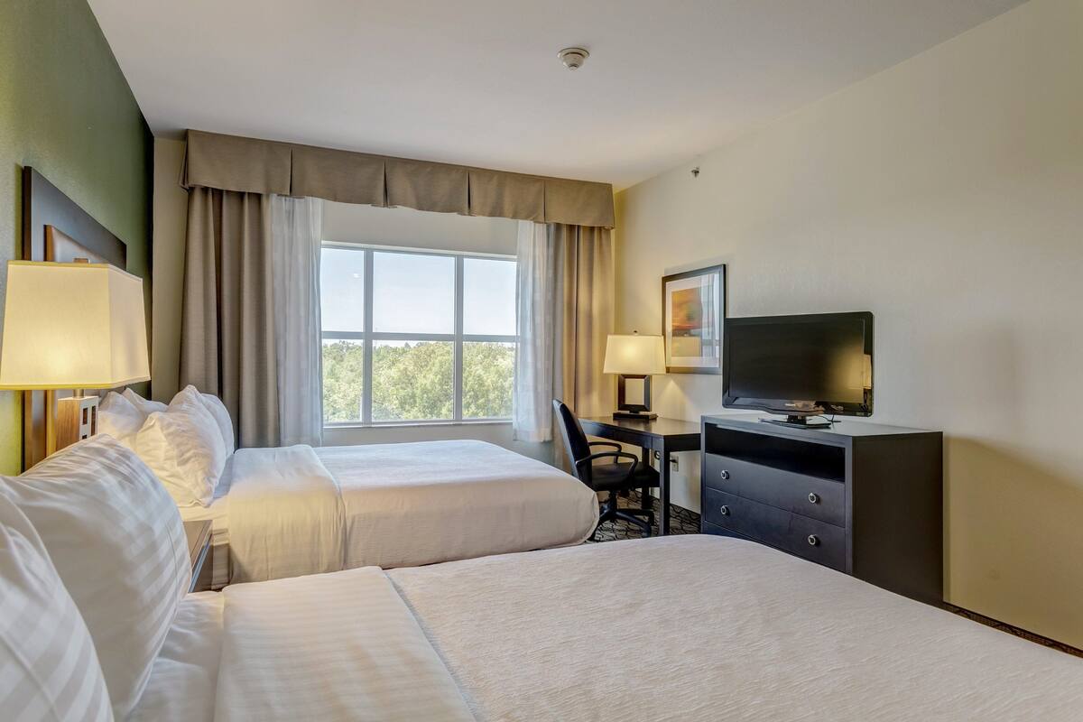A hotel room with two beds, a desk, a chair, a television, and a window with curtains.
