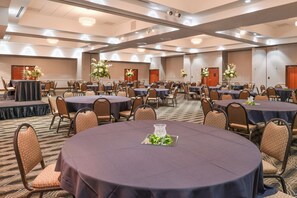 Un salón de conferencias con mesas y sillas redondas, decorado con centros de mesa florales.