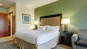 A hotel room with a large bed, two bedside tables with lamps, a chair, and a door.