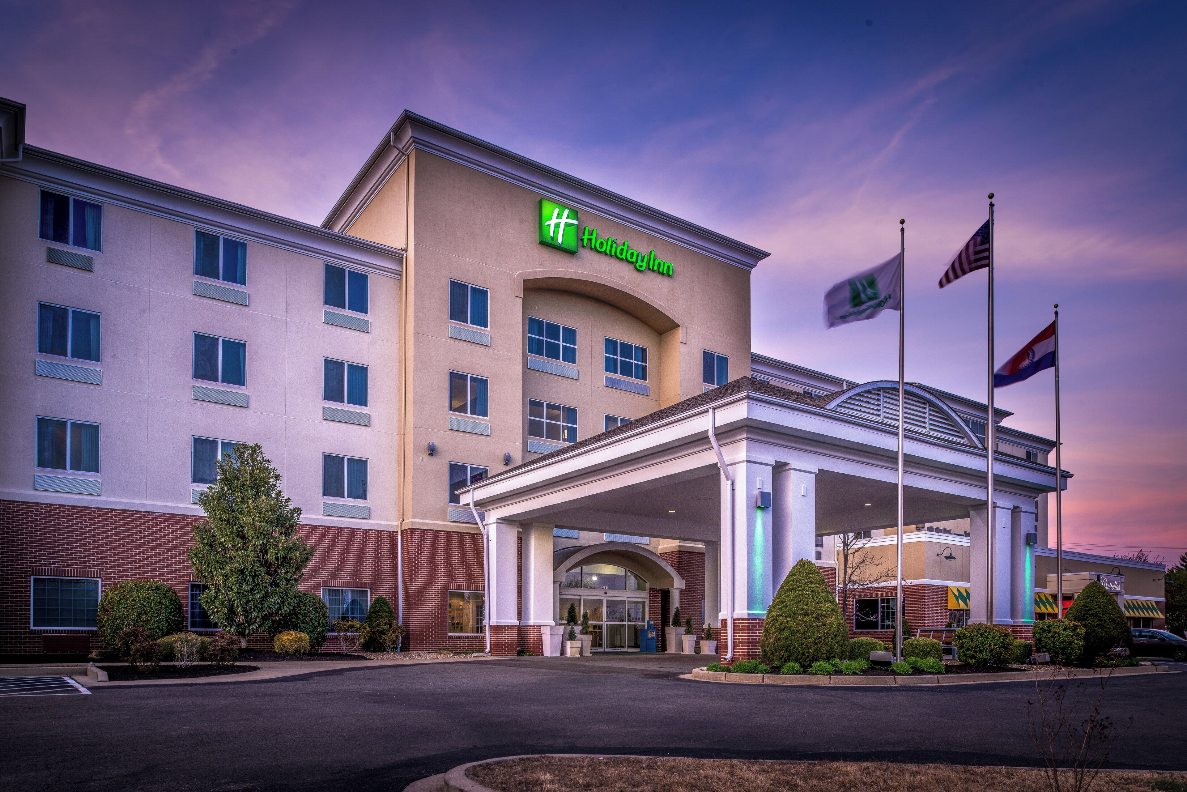 A Holiday Inn hotel with a covered entrance, multiple windows, and flags.