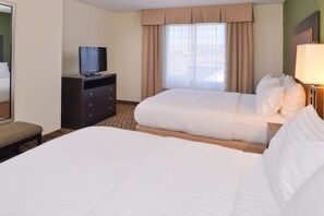 A hotel room with two beds, a TV on a dresser, and a window with curtains.
