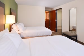 A hotel room with two beds, a bedside lamp, a bench, a mirror, and a door leading to another room.