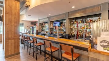 Zona de bar con una barra larga, varios taburetes y una amplia selección de botellas y vasos.